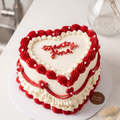 Heart-shaped cake with red and white icing on a white surface.